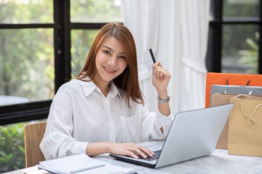 Güzel Çekici Asyalı kadın çevrimiçi alışveriş için kredi kartını kullanıyor çevrimiçi ödemeye dönüşüyor. Keyif ve mutluluk, alışveriş kavramı.