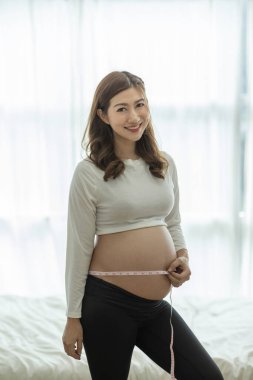 Güzel, Çekici Asyalı hamile kadın göbeğini ölçerek gülümsedi. Gurur ve mutluluk hissetti. Sağlıklı hamilelik kavramı, Seçici Odaklanma.