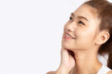 Çekici, çekici Asyalı genç bir kadın beyaz dişleriyle gülümsüyor ve yumuşak yanaklarına dokunuyor. Mutluluk ve neşe dolu, sağlıklı cilt, beyaz arka planda izole edilmiş, güzellik kavramı.