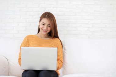 Güzel, Çekici Asyalı kadın beyaz koltukta bilgisayar laptopuyla çalışıyor ve iş hayatında fikir ve gereksinim edinmeyi düşünüyor.