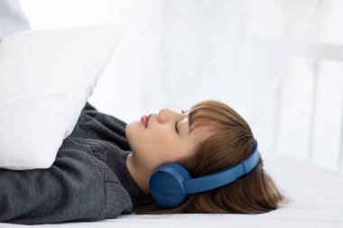 Güzel, çekici, Asyalı genç bir kadın müzik dinler ve yatak odasında uzanır. Rahat ve rahat hisseder. Yatak odası konsepti, seçici odaklanma.