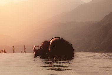 Kadın yogaya hazırlanıyor. Sabah dağın zirvesinin üstündeki havuzda poz veriyor. Güzel doğa manzaralarının önünde.