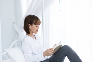 Güzel, çekici Asyalı kadın yatak odasında oturmuş öğrenme ve eğitim için kitap okuyor gülümseme ve olumlu düşünce çok mutlu ve rahat, Eğitim Konsepti