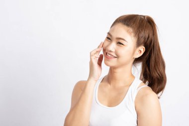 Çekici, çekici Asyalı genç bir kadın beyaz dişleriyle gülümsüyor ve yumuşak yanaklarına dokunuyor. Mutluluk ve neşe dolu, sağlıklı cilt, beyaz arka planda izole edilmiş, güzellik kavramı.