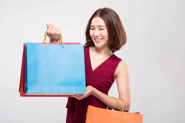 赤のドレスを着た短い髪の笑顔を持つショッピングアジアの女性ショッピングバッグを保持 陽気と幸福は黒の金曜日の販売で買い物を楽しむ 灰色の背景に隔離された — ストック写真