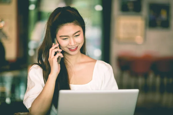 美しい魅力的なアジアの女性は ノートパソコンの笑顔で作業し コーヒーショップでのオフィス外での成功のためのアイデアや要件を得るためにスマートフォンで顧客と話す ビジネスコンセプト 暖かいトーン — ストック写真