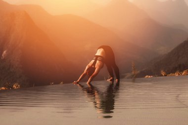 Çekici Asyalı kadın yoga yapıyor. Aşağı bakan köpek ya da Adho Mukha Svanasana poz veriyor. Sabah dağın zirvesinin üstündeki havuzda.