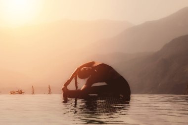 Kadın yogaya hazırlanıyor. Sabah dağın zirvesinin üstündeki havuzda poz veriyor. Güzel doğa manzaralarının önünde.