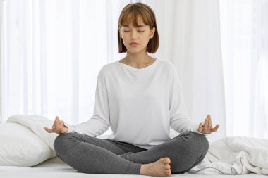Çekici Asyalı kadın yoga nilüferine poz veriyor. Sabah uyandıktan sonra yatakta meditasyon yapıyor. Kendini çok rahat ve rahat hissediyor.