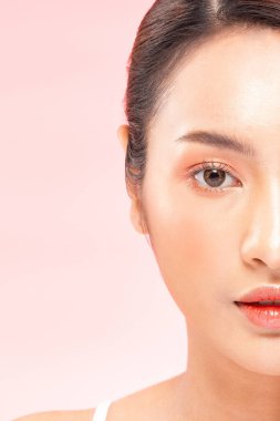 Güzel Asyalı kadının yarısı kameraya bakıp gülümsüyor. Temiz ve taze tenli. Mutluluk ve neşe, olumlu duygusal, pembe arka planda izole edilmiş, güzellik kozmetik ve kaplıca konsepti.