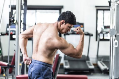 Vücut geliştiren yakışıklı Asyalı erkekler spor salonunda poz veriyorlar. Vücut geliştirme egzersizinden sonra kendilerini çok güçlü ve güçlü hissediyorlar.