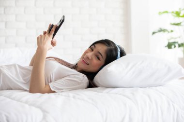 Güzel, çekici, Asyalı genç bir kadın müzik dinler ve yatak odasında uzanır. O yüzden rahatla ve rahatla, Seçici Odaklan.