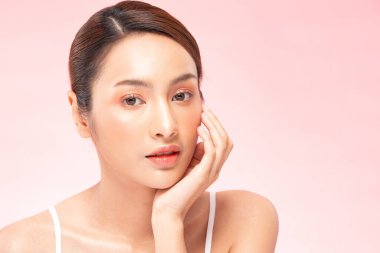Güzel Asyalı kadın, yumuşak yanaklı gülümsemeye, temiz ve taze tenli mutluluğa, olumlu duygulara, pembe arka plana, güzellik kozmetiğine ve kaplıcaya dokunuyor.