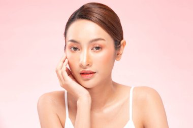 Güzel Asyalı kadın, yumuşak yanaklı gülümsemeye, temiz ve taze tenli mutluluğa, olumlu duygulara, pembe arka plana, güzellik kozmetiğine ve kaplıcaya dokunuyor.