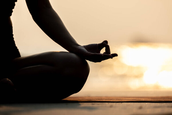 Silhouette Close up hand of woman practice yoga meditation lotus pose on the beach in thailand,Feeling so comfortable and relax in holiday with golden light,Healthy Concept,warm tone