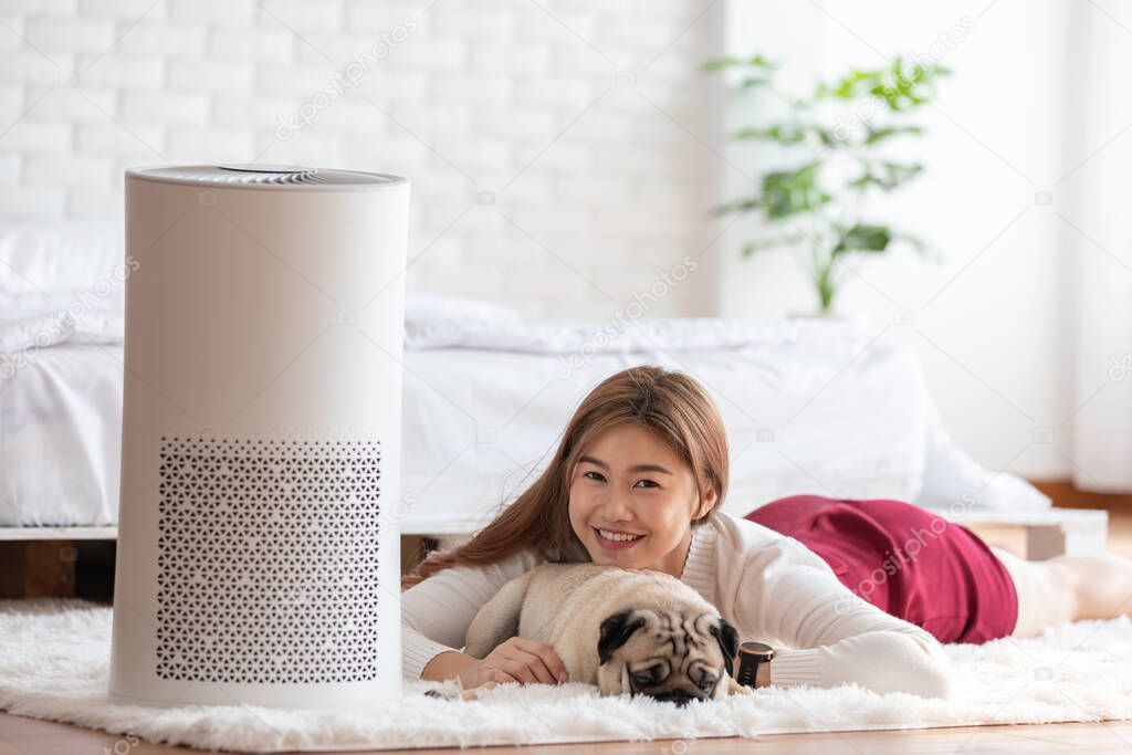 Woman playing with Dog Pug Breed and Air purifier in cozy white bed room for filter and cleaning removing dust PM2.5 HEPA in home,for fresh air and healthy life,Air Pollution Concept