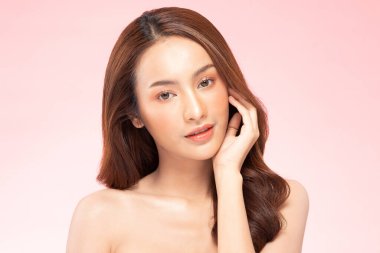 Güzel Asyalı kadın, yumuşak yanaklı gülümsemeye, temiz ve taze tenli mutluluğa, olumlu duygulara, pembe arka plana, güzellik kozmetiğine ve kaplıcaya dokunuyor.