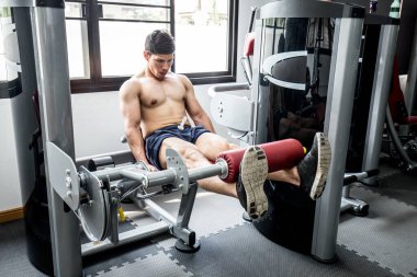 Asyalı yakışıklı adam spor salonunda üst bacak egzersizinde kas geliştirmek için bacak egzersizi yapıyor. Çok güçlü ve güçlü hissediyor, vücut geliştirici kavram.