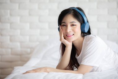 Güzel, çekici, Asyalı genç bir kadın müzik dinler ve yatak odasında uzanır. O yüzden rahatla ve rahatla, Seçici Odaklan.