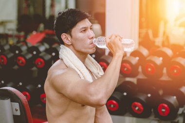 Spor salonunda çalıştıktan sonra içme suyu tutan yakışıklı Asyalı genç adamlar serinlemek ve kasları güçlü vücutta gevşetmek, vücut geliştirici kavram.