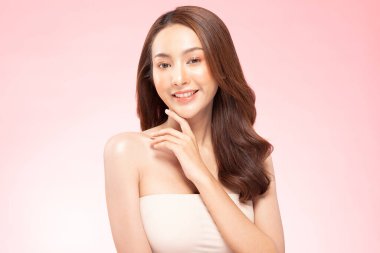 Güzel Asyalı kadın gülümsüyor temiz ve taze tenli çeneye dokunuyor mutluluk ve neşe olumlu duygusal, pembe arka planda izole edilmiş güzellik kozmetik ve kaplıca konsepti