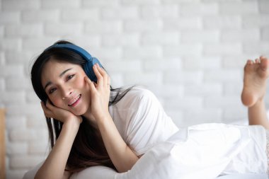 Güzel, çekici, Asyalı genç bir kadın müzik dinler ve yatak odasında uzanır. O yüzden rahatla ve rahatla, Seçici Odaklan.