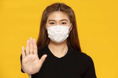 woman waring protection mask from coronavirus and air pollution making stop hand sign isolated on yellow background,Health care concept clipart
