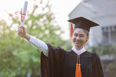 Çekici Asyalı Kadın Öğrenci Başlık ve cübbe ile mezuniyet töreni elinde sertifikayla ve gurur verici bir mutlulukla Mezuniyet Günü 'nde öğrenciyi ve Eğitim Başarı' nı kutluyor.