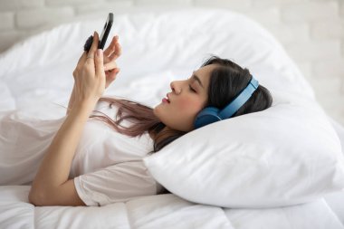 Güzel, çekici, Asyalı genç bir kadın müzik dinler ve yatak odasında uzanır. O yüzden rahatla ve rahatla, Seçici Odaklan.