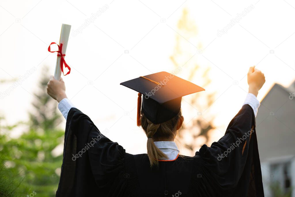 Back of view Graduate put hands up and celebrating with certificate in her hand and so proud and happiness in Commencement day,Congratulation of student in graduation day,Education Success Concept