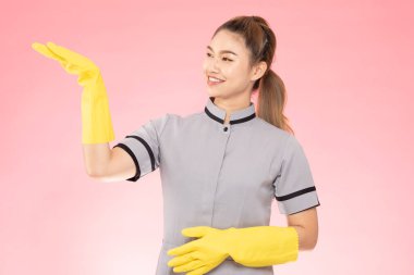 Çekici, güzel Asyalı kadın, eldivenli, gülümseyen ve açık avuçlu bir tabela ile ürünleri gösteren mutlu ve kendinden emin, pembe arka planda izole, temizlik hizmeti kavramına sahip.