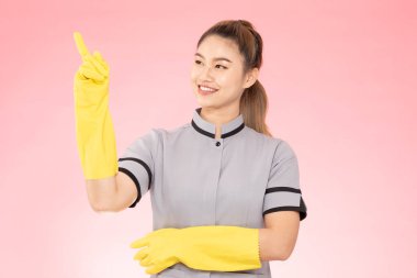 Çekici, güzel Asyalı kadın, eldivenli, gülümseyen, işaret eden, mutlu ve kendinden emin, pembe arka planda izole edilmiş, temizlik hizmeti konsepti olan.