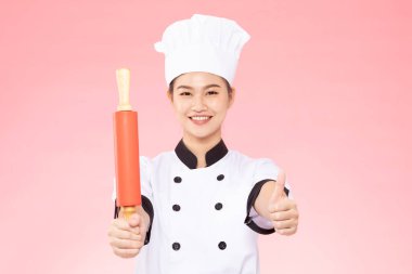 Güzel Asyalı şef kadın gülümsüyor ve pembe arka planda izole edilmiş oklavaları tutuyor, Mutluluk ve Neşeli Profesyonel Şef Konsepti
