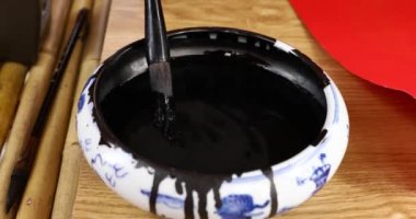 Yeni yılda kırmızı kağıda yazı yazmak. Su seviyesini fırça ve mürekkeple daldır. Asyalıların yazı aletleri. Antik Asya yazıları. Asya yazı stili. Kırmızı kağıt. 4K video