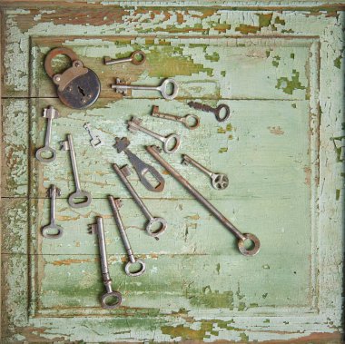 Eski ahşap bir yüzey üzerinde eski bir anahtar deliği ve eski vintage anahtarlar bulunan eski bir kilit. Ahşap dokular soyulmuş yeşil boyalardan görülebiliyor..