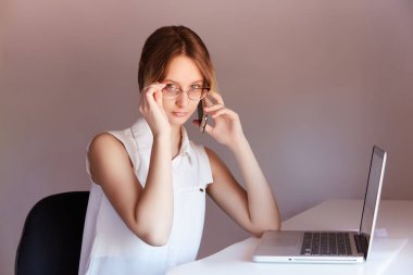 Öğleden sonra masada konuşan ve telefona bakan gözlüklü bir kız. Çevrimiçi öğrenci olarak çalış.