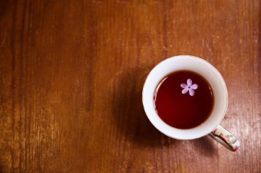 Eski ahşap bir masada kupada çay. Çayda leylak çiçeği
