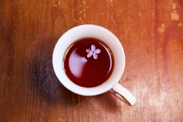 Tea in a mug on an old wooden table. Lilac flower in tea