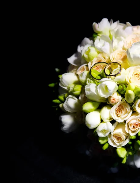 The bride\'s bouquet on a black background is one. wedding bouquet and two gold rings, the rings are on the flower buds in the bouquet.