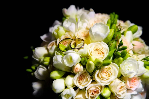 The bride\'s bouquet on a black background is one. wedding bouquet and two gold rings, the rings are on the flower buds in the bouquet.