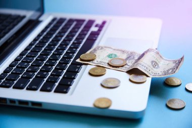 Kağıt ve demir para mavi bir masadaki dizüstü bilgisayarın klavyesinde. Kâr, kredi, ofiste banka bilgileri, büyük bir iş planı, internetten uzaktan çalışma kavramı..