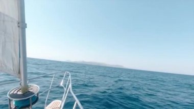 Hafta sonu sıcak bir günde, derin mavi bir okyanusun ortasındaki adaya doğru giden büyük bir yatla Aigina Yelkenli Gezisi. Atış, teknede durarak elde yapılmış..