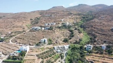 Yunanistan 'ın Tinos kentindeki tepede çok az sayıda ev bulunan kuru dağ manzarasına doğru insansız hava aracı uçuşu