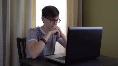 4 bin. Gözlüklü çalışkan bir genç bir masada oturuyor ve bir dizüstü bilgisayarda ödev yapıyor, internetten bilgi öğreniyor..