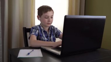 4 bin. İşaretli gömlekli bir öğrenci, dizüstü bilgisayar kullanarak, evde oturarak ve bilgisayar ekranında dikkatlice bilgi okuyarak ödevini başarıyla yapıyor. İnternet teknolojisi .