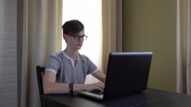 4 bin. Gözlüklü çalışkan bir genç bir masada oturuyor ve bir dizüstü bilgisayarda ödev yapıyor, internetten bilgi öğreniyor..