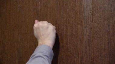 Kahverengi ahşap kapıya yumruk atan bir adamın yan görüntüsü. Elin yakınına. .