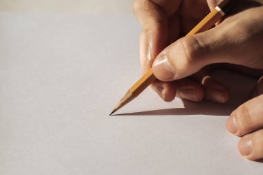 Beyaz arka planda izole edilmiş bir kalem tutan bir adam. Elleri kurşun kalemle bir şeyler yazıyor.