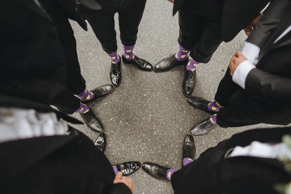 Feet of the groom and friends of the groom with funny colored socks. Men in colorful socks and black shoes. They stand in a circle. FASHION, STYLE, BEAUTY.