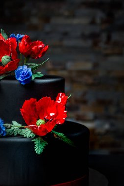 Siyahlı iki katlı güzel bir pasta. Haşhaş ve mısır çiçekleriyle süslenmiş. Kırmızı ve mavi çiçekler. Çok etkili bir süs.